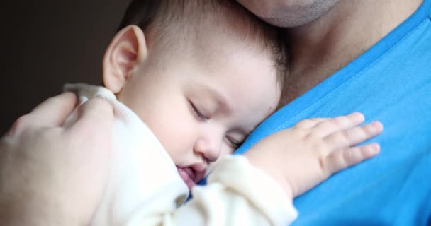 Ένα μικρό παιδί αποκοιμήθηκε στην αγκαλιά του πατέρα του. Ο μπαμπάς κουνάει το μωρό για να κοιμηθεί. Κοντινό πλάνο. 4ια — Αρχείο Βίντεο