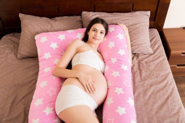 Genç hamile bir kadın destek yastığıyla yatakta yatıyor..