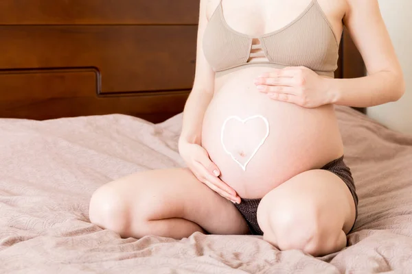 Μια Έγκυος Κάθεται Στο Κρεβάτι Και Πασαλείβει Την Καρδιά Της — Φωτογραφία Αρχείου