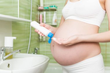 Genç hamile bir kadın sabah banyoda karnına gerilme önleyici krem sürüyor. Hamilelik, annelik ve vücut bakımı kavramı .