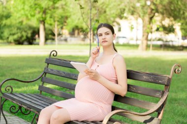 Hamile kadın parkta bir bankta oturuyor ve hastaneye yapılacaklar listesi yazıyor..