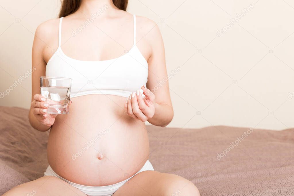 woman holding pill and glass of fresh pure water. Healthy millennial women taking antioxidant medicine vitamins, healthcare concept.