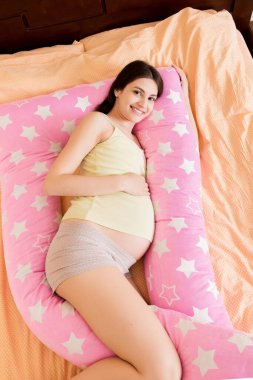 Genç hamile bir kadın destek yastığıyla yatakta yatıyor..