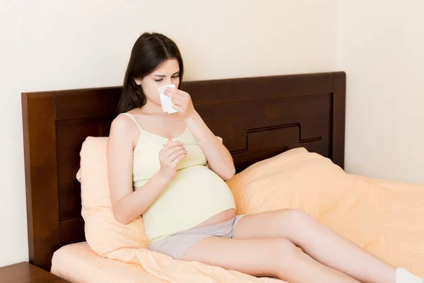 若い不幸な妊婦の肖像ベッドの上で枕にもたれ 組織に彼女の鼻を吹いて 未来のお母さんキャッチ寒さとくしゃみ — ストック写真