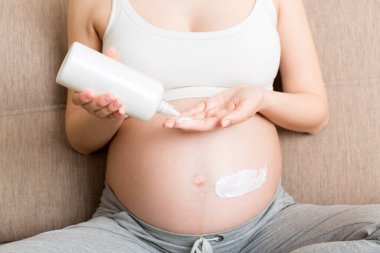 Hamile bir kadın karnına krem sürüyor. Hamilelik, insanlar ve annelik kavramı. Hamileyken karnına gerilme önleyici krem sür..