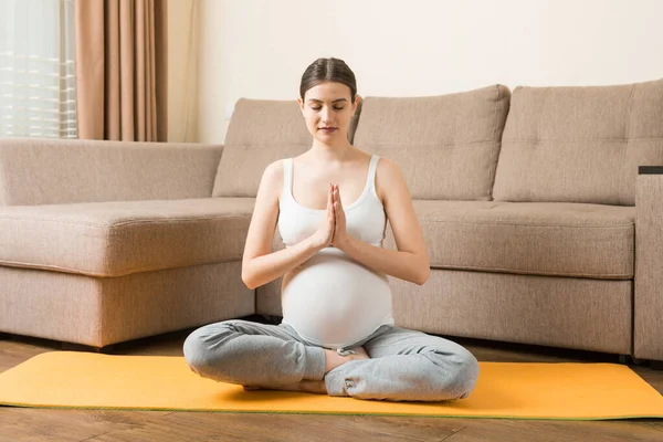 Pregnancy Yoga and Fitness concept at coronavirus time. Pregnant woman meditates indoor in yoga pose. Woman enjoying in meditation.