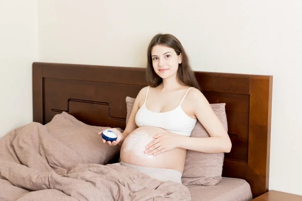 Una Chica Embarazada Sienta Casa Cama Frota Sonrisa Una Crema —  Fotos de Stock