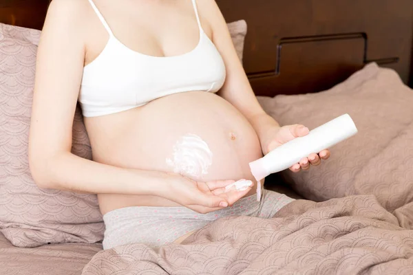 pregnant woman applying stretch mark cream to belly. pregnancy, people and maternity concept. pregnant apply anti-stretch mark cream on her belly.