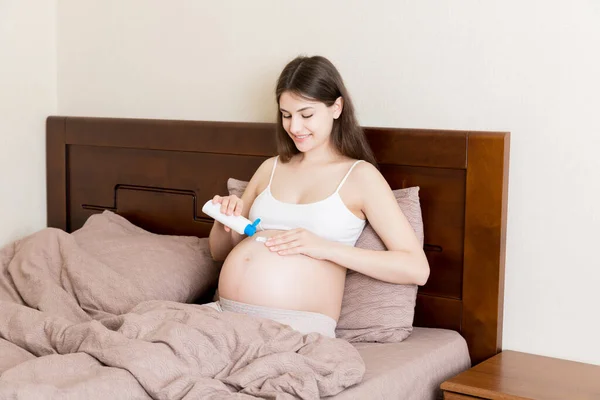 Una Chica Embarazada Sienta Casa Cama Frota Sonrisa Una Crema —  Fotos de Stock