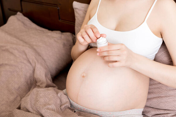 pregnant woman applying stretch mark cream to belly. pregnancy, people and maternity concept. pregnant apply anti-stretch mark cream on her belly.