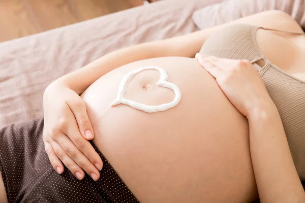 Μια Έγκυος Κάθεται Στο Κρεβάτι Και Πασαλείβει Την Καρδιά Της — Φωτογραφία Αρχείου