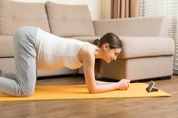 Mujer Embarazada Sosteniendo Teléfono Inteligente Mientras Está Sentada Esterilla Yoga — Foto de Stock