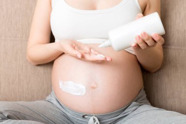 Hamile bir kadın karnına krem sürüyor. Hamilelik, insanlar ve annelik kavramı. Hamileyken karnına gerilme önleyici krem sür..