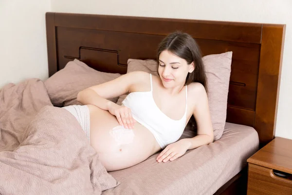 Egy Terhes Lány Otthon Ágyon Egy Nyúlásgátló Krémet Kent Hasára — Stock Fotó