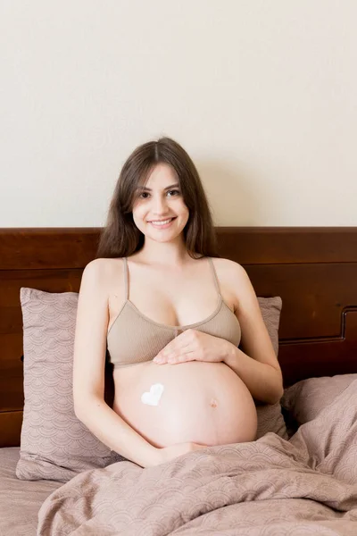 Egy Terhes Lány Otthon Ágyon Egy Nyúlásgátló Krémet Kent Szívére — Stock Fotó