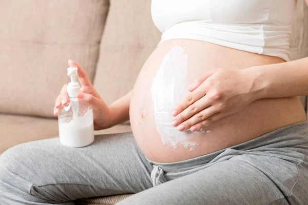 pregnant woman applying stretch mark cream to belly. pregnancy, people and maternity concept. pregnant apply anti-stretch mark cream on her belly.