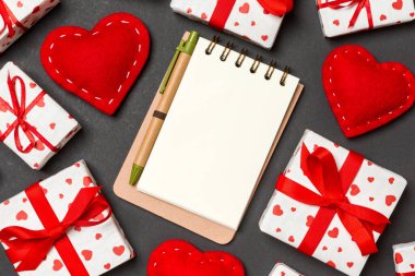 Defterin üst görüntüsü, beyaz hediye kutuları ve renkli arka planda kırmızı tekstil kalpleri. Sevgililer Günü konsepti.