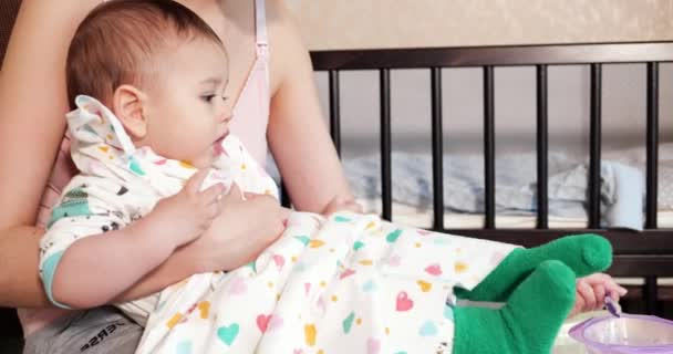 Mãe segura o bebê em seus braços e alimenta seu filho com uma colher. conceito de família, alimentação, criança, alimentação e paternidade — Vídeo de Stock