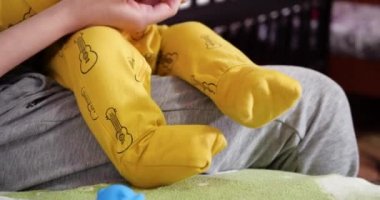 Genç bir anne kucağında küçük bir çocukla yatakta oturur ve oyunu bir ip ve diğer dokunsal oyuncaklarla kontrol eder. Annelik, annelik ve aile kavramı