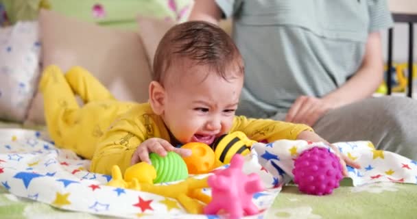 Η μαμά χαϊδεύει το μωρό όταν ξαπλώνει στο κρεβάτι με ένα παιχνίδι οδοντοφυΐας. — Αρχείο Βίντεο