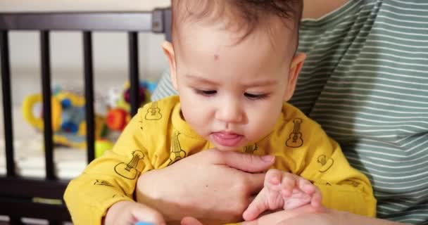 Eine junge Mutter sitzt mit einem kleinen Kind im Arm auf dem Bett und steuert das Spiel mit einem Beißring und anderen taktilen Spielzeugen. Mutterschaft, Mutterschaft und Familienkonzept — Stockvideo