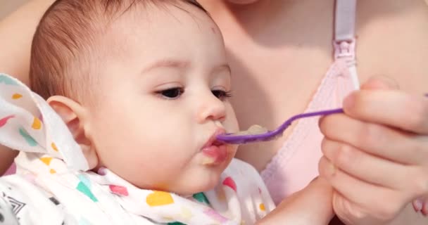 Mãe segura o bebê em seus braços e alimenta seu filho com uma colher. conceito de família, alimentação, criança, alimentação e paternidade — Vídeo de Stock