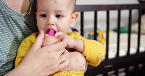 Una giovane madre siede sul letto con un bambino piccolo tra le braccia e controlla il gioco con un etere e altri giocattoli tattili. Maternità, maternità e concetto di famiglia — Video Stock