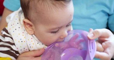 Anne bebeği kollarında tutuyor ve oğlunu kaşıkla besliyor. aile, yemek, çocuk, yeme ve ebeveynlik kavramı