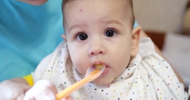 Anne bebeği kollarında tutuyor ve oğlunu kaşıkla besliyor. aile, yemek, çocuk, yeme ve ebeveynlik kavramı