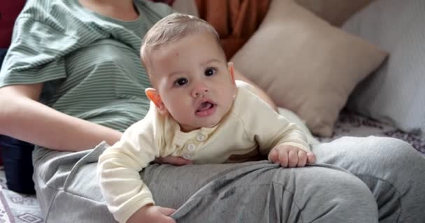 Een jonge moeder houdt een mooie zeven maanden oude zoon vast die glimlacht en knaagt aan vingers en moeders hand. jeukende tanden van een pasgeborene, tandjes krijgen — Stockvideo