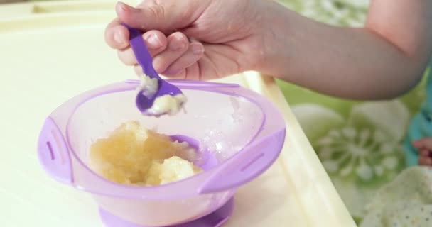 Mère tient le bébé dans ses bras et nourrit son fils avec une cuillère. famille, nourriture, enfant, alimentation et concept de parentalité. au ralenti — Video