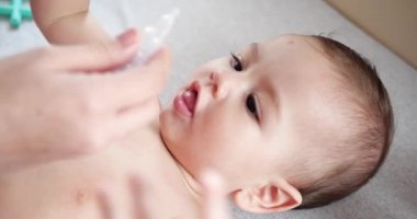 Bebek yalan söyleyip gülümserken anne bebeğin burnuna damlatıyor. Burnunu sümükten temizlemek