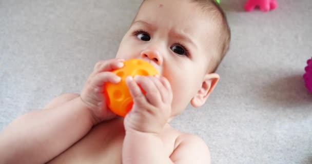Säugling, Kindheitskonzept - Nahaufnahme eines lächelnden glücklichen Babys, das mit einem Beißring spielt. Zähne zusammenbeißen. Erste Zähne. Joy zahnlos 7 Monate Baby-Biss, nagt Beißspielzeug — Stockvideo