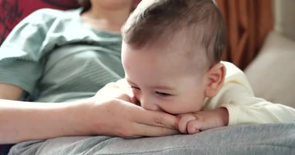 Een jonge moeder houdt een mooie zeven maanden oude zoon vast die glimlacht en knaagt aan vingers en moeders hand. jeukende tanden van een pasgeborene, tandjes krijgen — Stockvideo