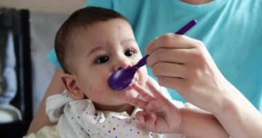 Anne bebeği kollarında tutuyor ve oğlunu kaşıkla besliyor. aile, yemek, çocuk, yeme ve ebeveynlik kavramı