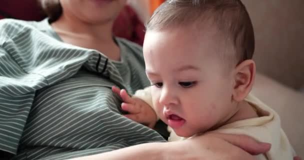 Una joven madre sostiene a un hermoso hijo de siete meses que sonríe y roe los dedos y las manos de las madres. picazón en los dientes de un recién nacido, dentición — Vídeos de Stock