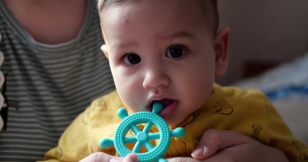 Seorang ibu muda duduk di tempat tidur dengan seorang anak kecil dalam pelukannya dan mengontrol permainan dengan teether dan mainan taktil lainnya. Persalinan, keibuan dan konsep keluarga. gerak lambat — Stok Video