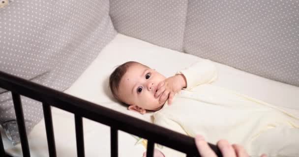 新生快乐的小宝宝在他的婴儿床里和乳头一起咀嚼和玩耍。滑稽的微笑透过婴儿床的栏杆看过去.慢动作 — 图库视频影像