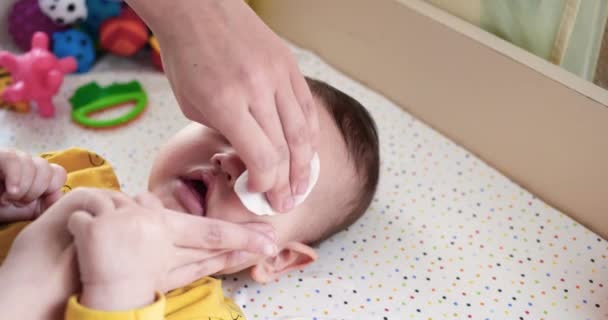 Zbliżenie matki czyszczącej twarz i oczy jej nowonarodzonego synka z podkładką. Matka wyciera dziecko mokrą podkładką z bawełny. zwolniony ruch — Wideo stockowe