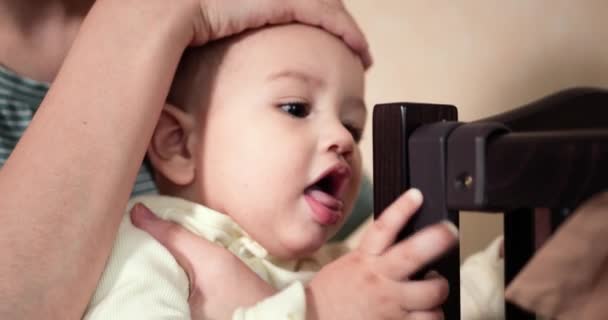 Barnet leker med barnsängen. Skär tänder. De första tänderna. 7 månader gammal baby biter, gnager hörnet av sängen i stället för teether. Ett barndomskoncept. slow motion — Stockvideo