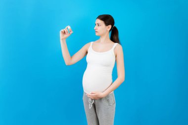 Hamile bir kadın karnına renkli arka planda fotokopi alanı olan bir şişe hap tutuyor. Hamilelik sırasında ilaç almak.