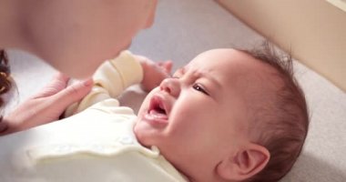 Annem ağlayan küçük bir çocuğu yatakta giydirir. Tıp, sağlık, aile masumiyeti, pediatri, mutluluk, bebek konseptleri. yavaş çekim