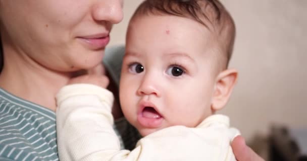 一位年轻的母亲抱着一个漂亮的7个月大的儿子，她笑着咬着手指和母亲的手。新生儿发痒的牙齿，牙疼。慢动作 — 图库视频影像