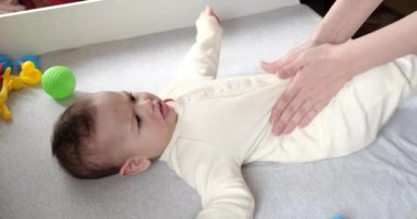 Anne küçük bebeğe masaj yapıyor. Bebek bakımı ve gelişim konsepti. Kolik önleme. Yeni doğan bebeğe karın masajı yapan kadın eller. yavaş çekim