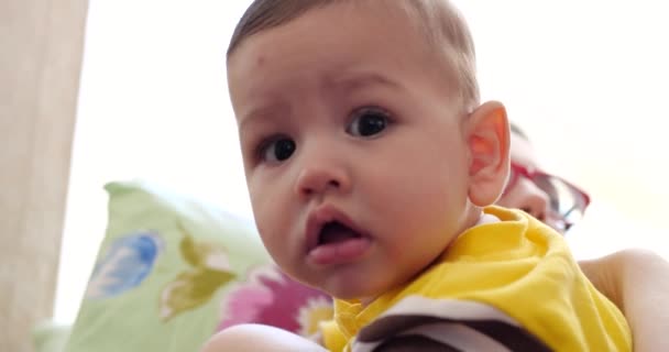 Eine junge Mutter hält einen schönen sieben Monate alten Sohn, der lächelt und an Fingern und Müttern nagt. Juckende Zähne eines Neugeborenen, Kinderkrankheiten. Zeitlupe — Stockvideo