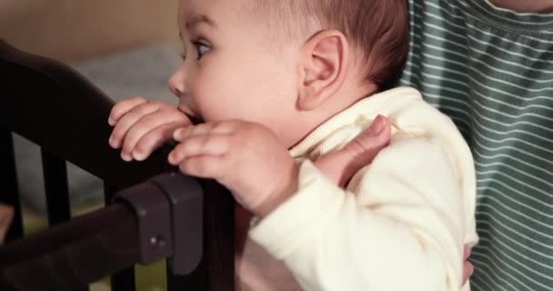 Dziecko bawi się łóżeczkiem. Wycinanie zębów. Pierwsze zęby. 7-miesięczne dziecko gryzie, gryzie róg łóżka zamiast ząbka. Dziecko, koncepcja dzieciństwa. zwolniony ruch — Wideo stockowe
