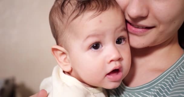 Een jonge moeder houdt een mooie zeven maanden oude zoon vast die glimlacht en knaagt aan vingers en moeders hand. jeukende tanden van een pasgeborene, tandjes. slow motion — Stockvideo