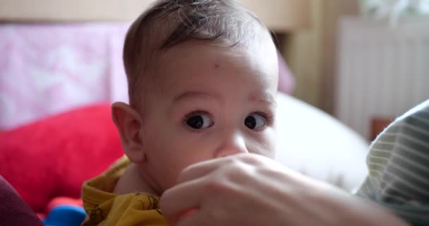 Eine junge Mutter hält einen schönen sieben Monate alten Sohn, der lächelt und an Fingern und Müttern nagt. Juckende Zähne eines Neugeborenen, Kinderkrankheiten. Zeitlupe — Stockvideo