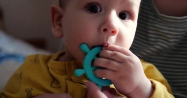 Genç bir anne kucağında küçük bir çocukla yatakta oturur ve oyunu bir ip ve diğer dokunsal oyuncaklarla kontrol eder. Annelik, annelik ve aile kavramı. yavaş çekim