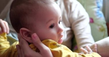 Genç bir anne, yedi aylık güzel bir oğlunu kucağında tutuyor ve gülümseyip, parmaklarını ve anne elini kemiriyor. Yeni doğmuş bir bebeğin dişleri kaşındırıyor. yavaş çekim